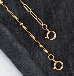Two styles of gold necklaces laying on a piece of slate