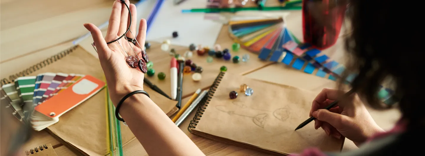 Jewelry artists sketching on note pad with holding up a pair of handmade earrings