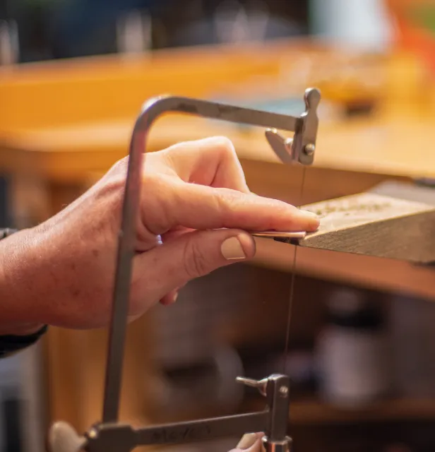 Jeweler sawing piece of sterling silver sheet at bench