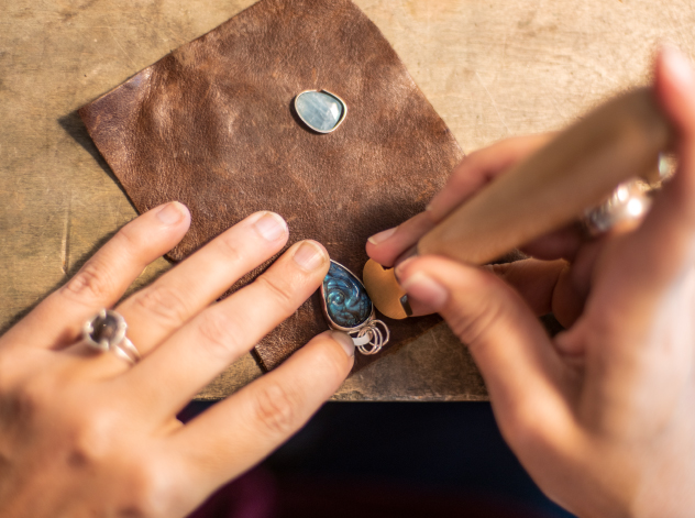 Top view of jeweler's bench with artists hands setting a blue stone in a sterling silver bezel