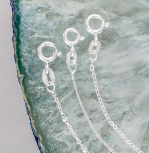 Three sterling silver chains with spring rings displayed on a light blue geode slice