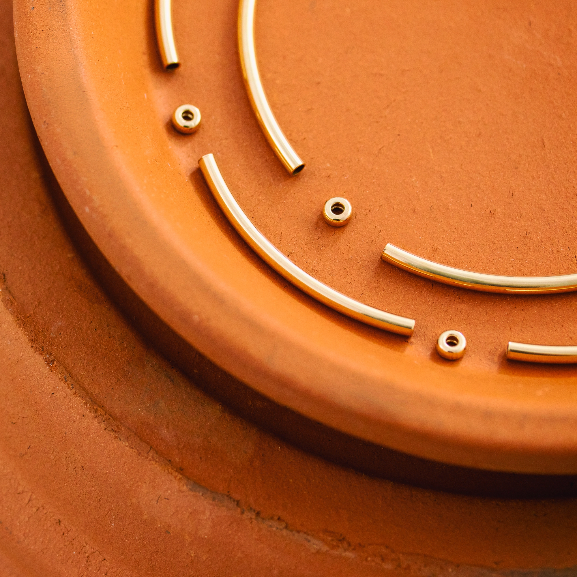Gold-filled jewelry beads and tubes laying on terracotta pot