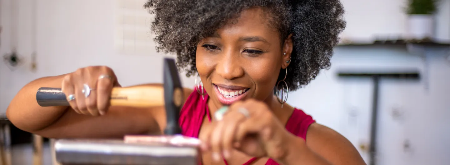 African American woman jeweler texturing a piece of metal with jewelry hammer