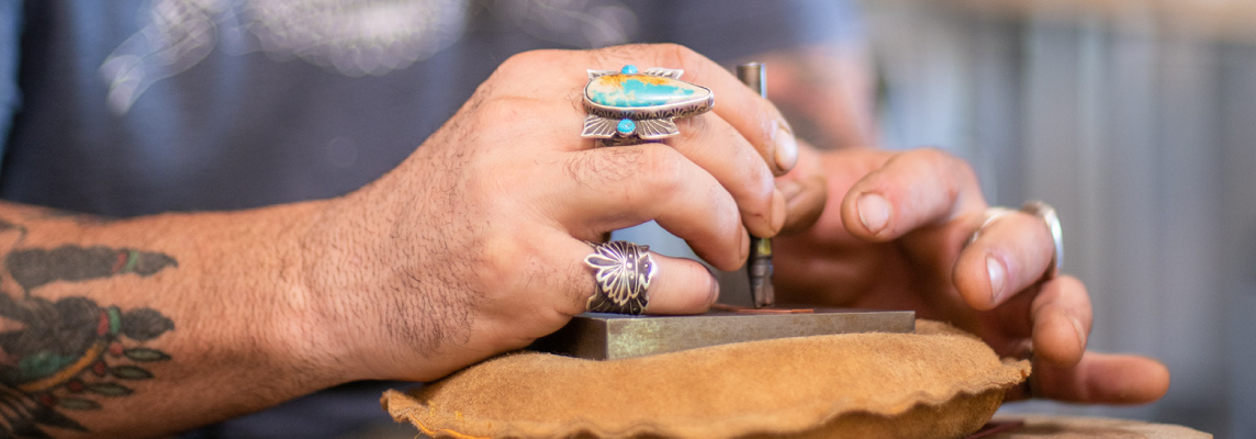 Male jeweler hands steadying a metal stamp to make an impression on sheet metal