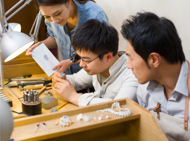 Three Asian students examining a bracelet at a jewelers bench