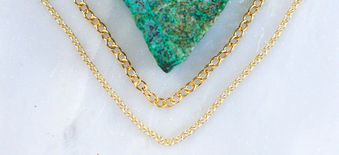 Two styles of gold-filled jewelry chain laying next to turquoise stone