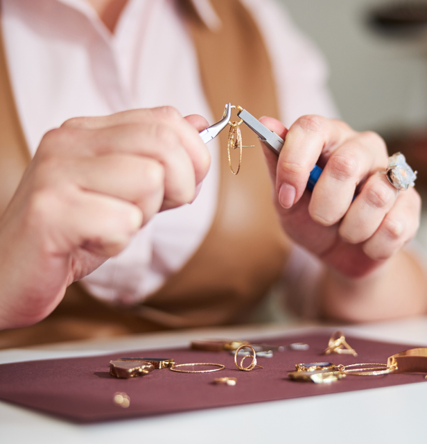 Women's hands holding jewelry pliers connecting a jump ring on an earring
